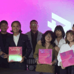 Team holding Shifting Sands branding project with bright pink background, showcasing brand identity work.