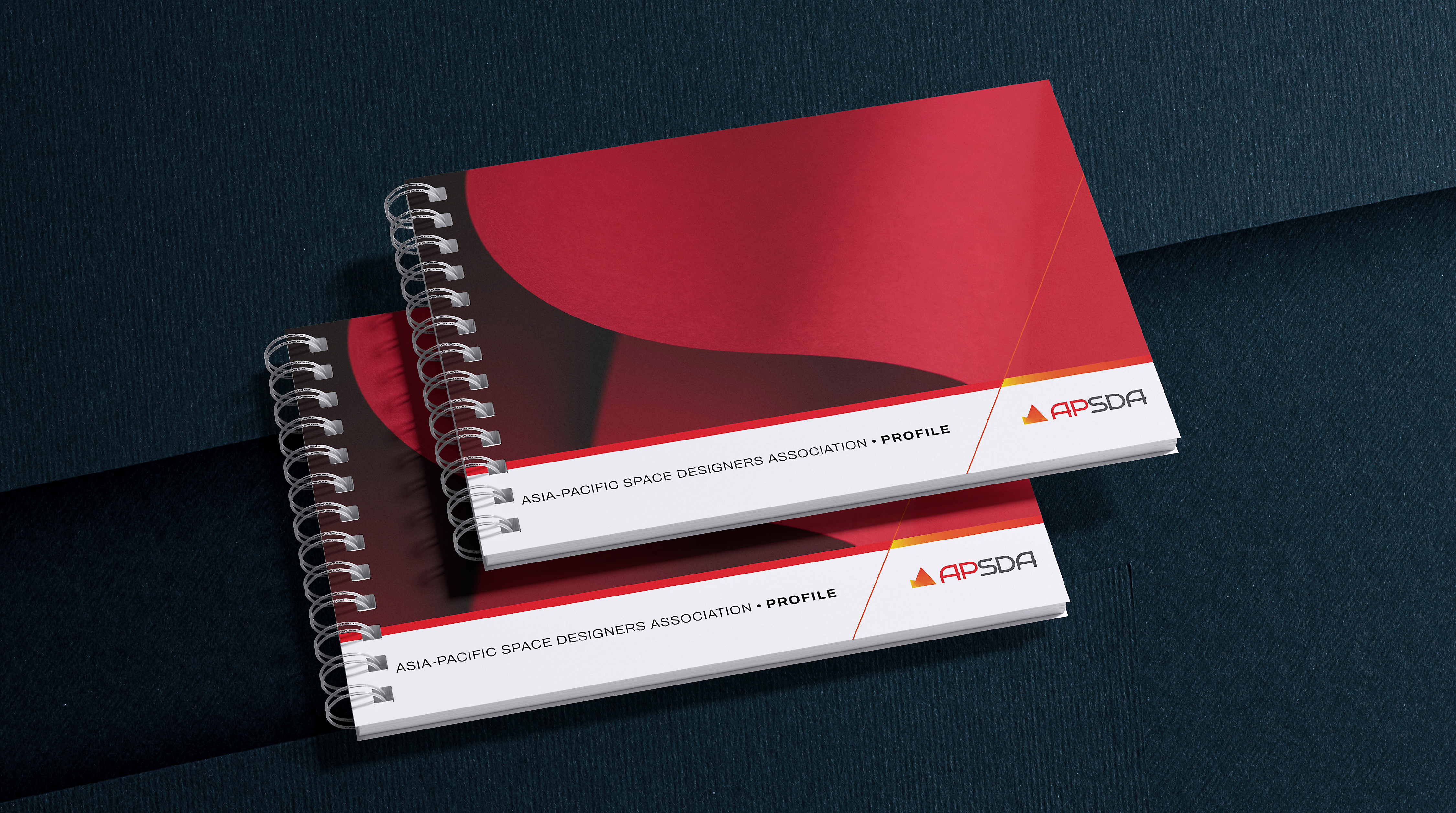 APSDA branding featuring spiral-bound books with red covers, showcasing visual identity and print design.