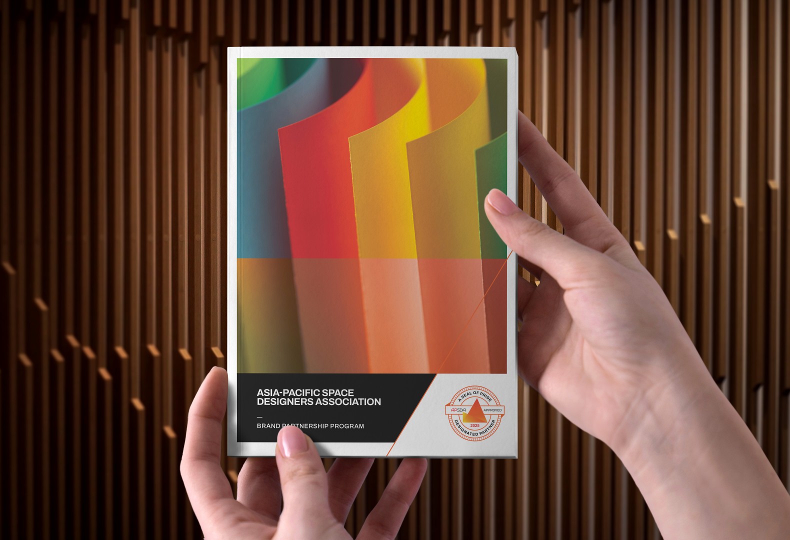 Hands holding colorful Asia-Pacific Space Designers Association branding booklet, showcasing visual identity design.