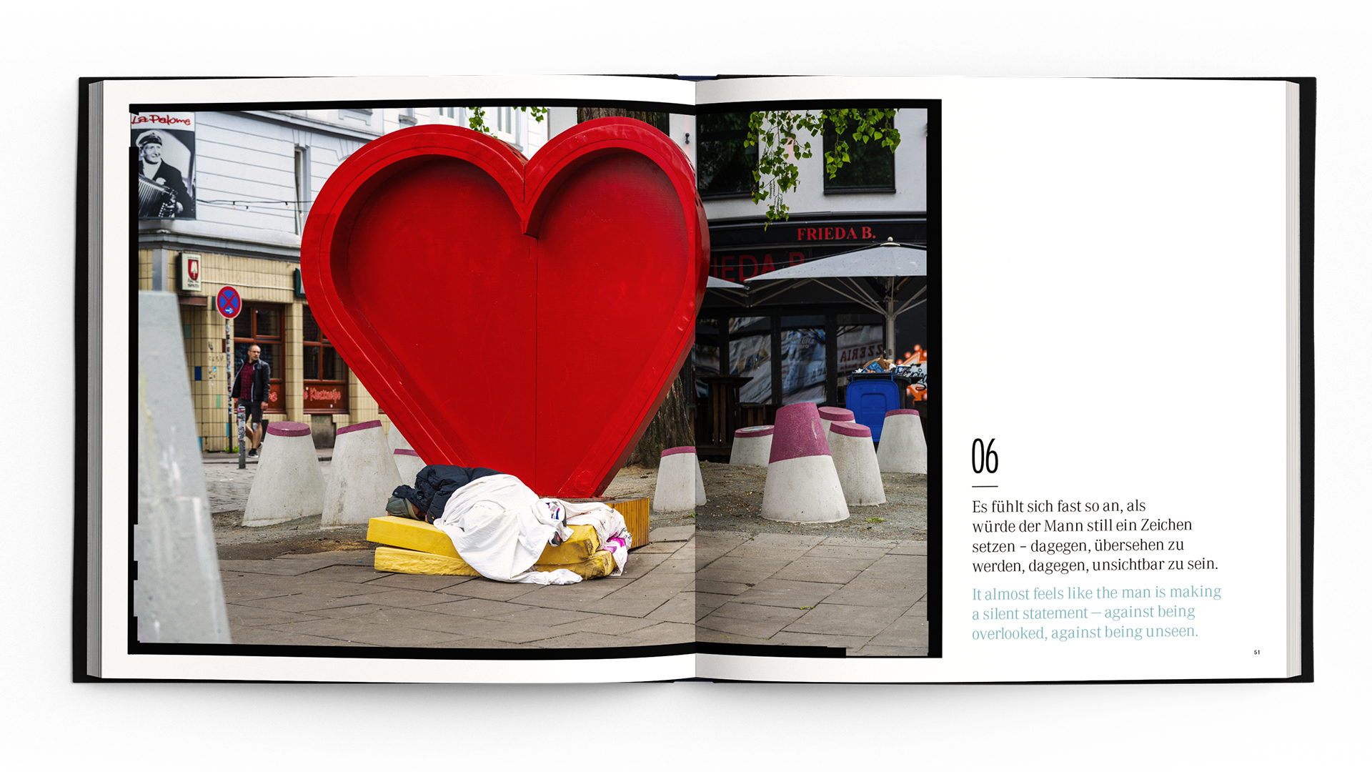 Open book with a street scene featuring a large red heart sculpture and a person resting beneath it.