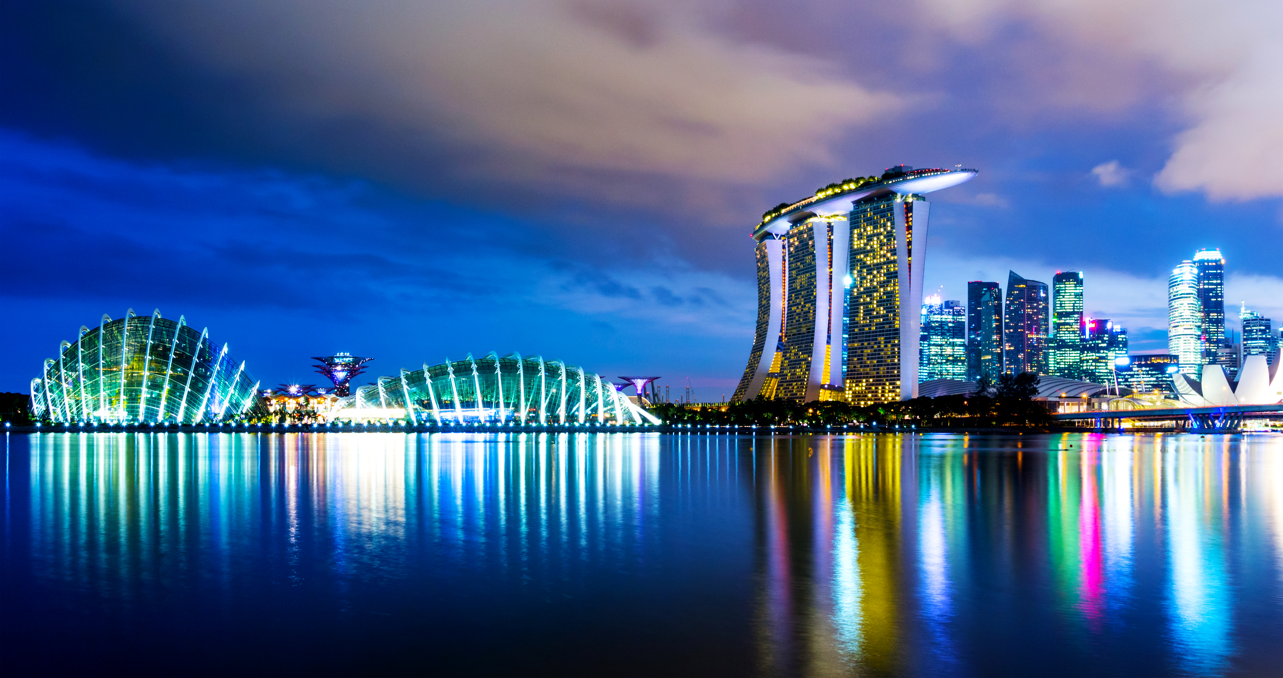 Singapore skyline at night with Marina Bay Sands and Gardens by the Bay, showcasing vibrant cityscape and reflection.