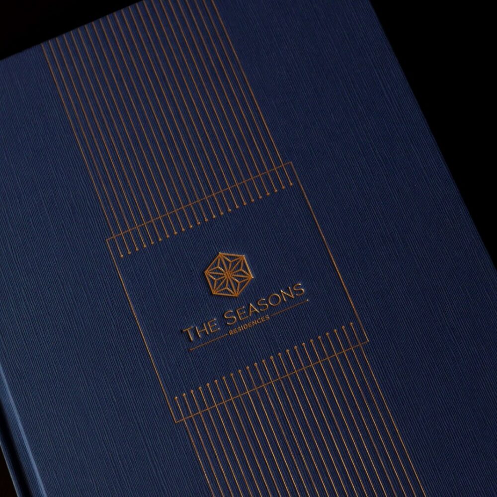 The Seasons branding on blue textured cover with gold geometric lines, showcasing refined visual identity design.