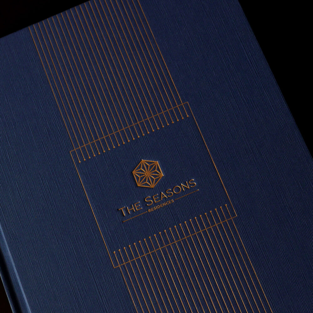 The Seasons Residences branding, featuring a navy and gold embossed cover design with geometric visual identity elements.