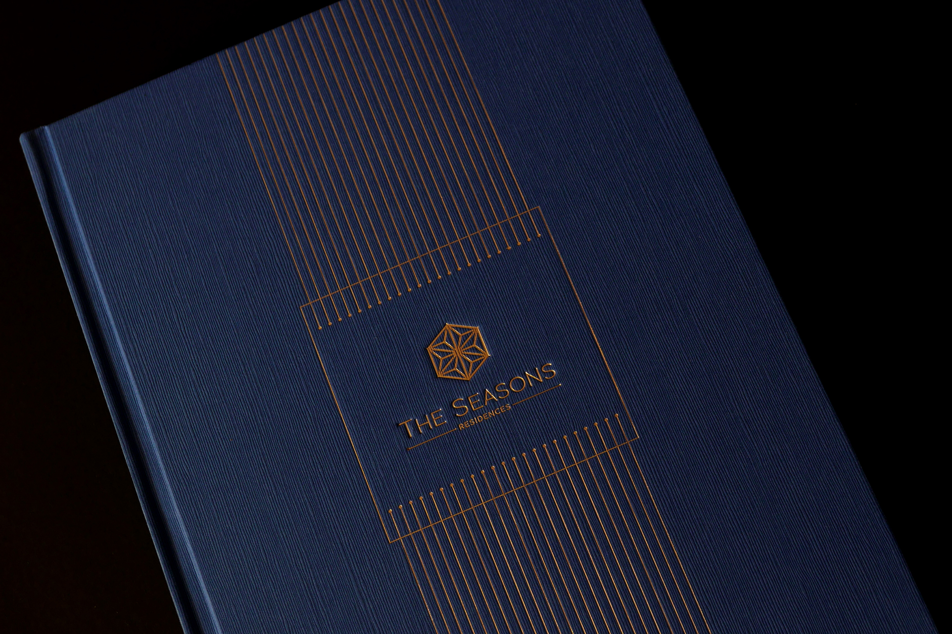 The Seasons Residences branding, featuring a navy and gold embossed cover design with geometric visual identity elements.