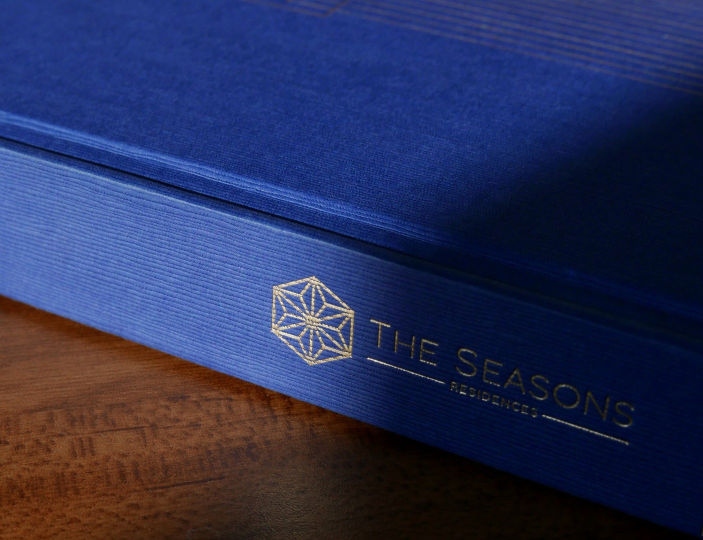 The Seasons Residences brand identity on blue textured packaging with gold geometric logo.