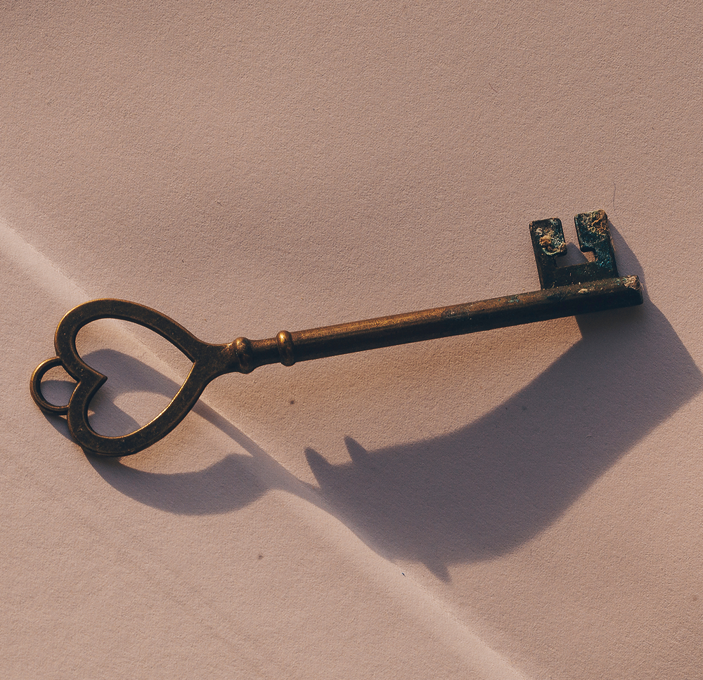 Antique key casting a shadow on a textured surface, symbolizing unlocking design potential in branding and visual identity.