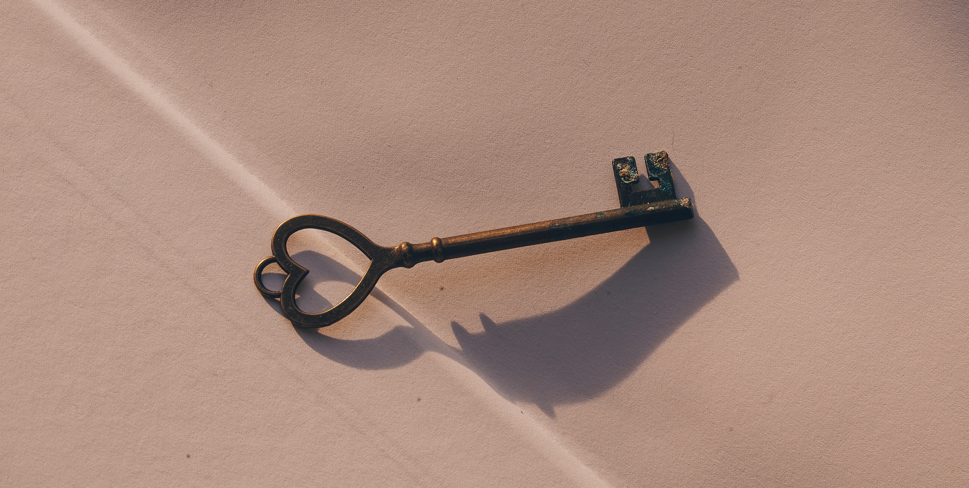 Antique key casting a shadow on a textured surface, symbolizing unlocking design potential in branding and visual identity.