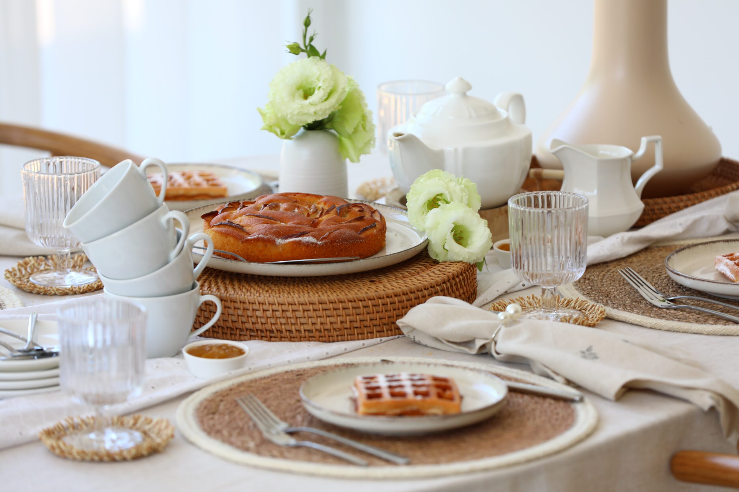 Breakfast table set with pastries, white crockery, and woven accents.