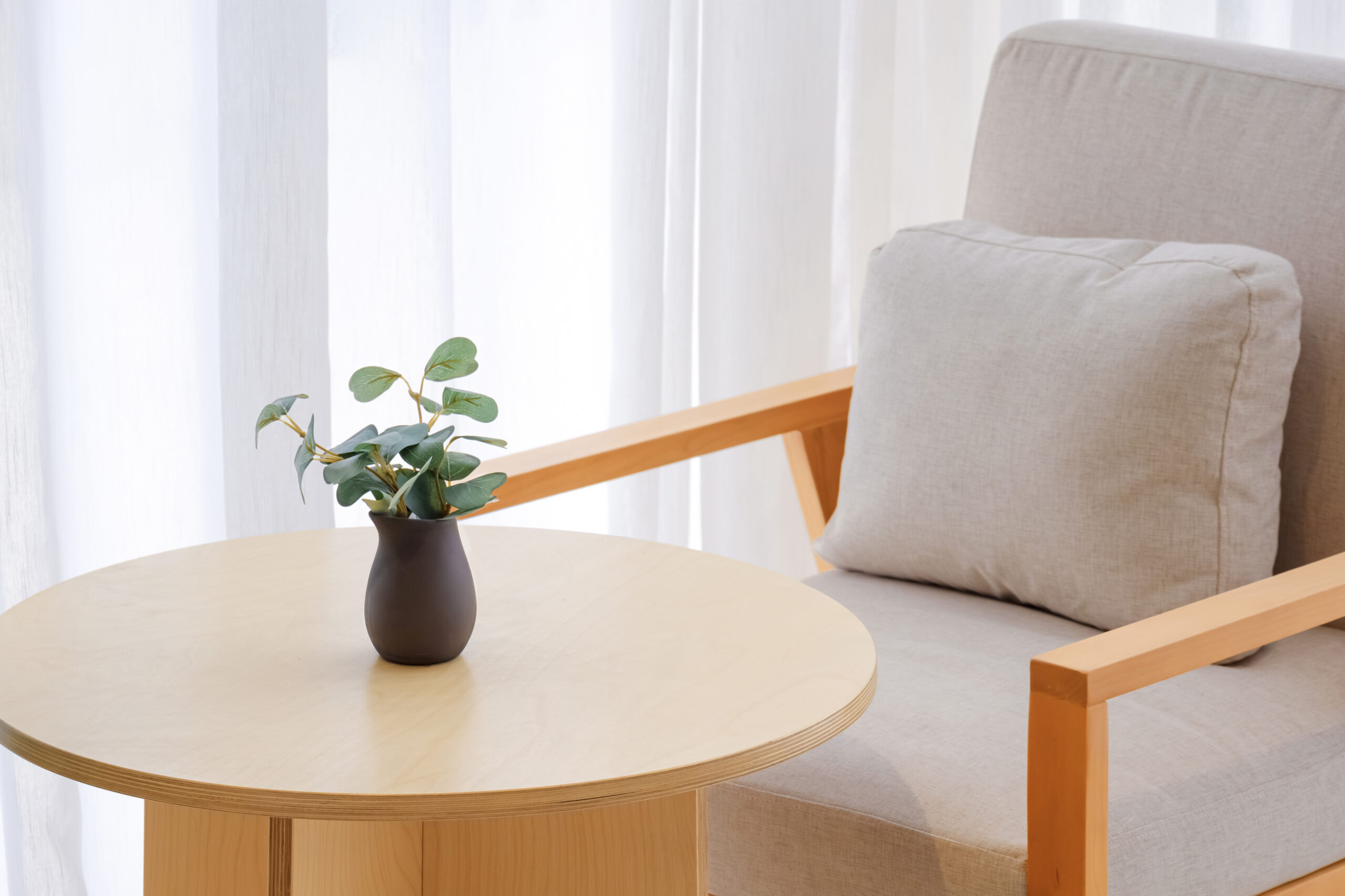Light wood chair beside a round table with a plant in a dark vase.